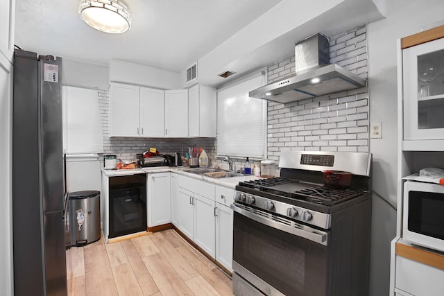 kitchen featuring white cabinets, wall chimney range hood, sink, light hardwood / wood-style floors, and stainless steel appliances