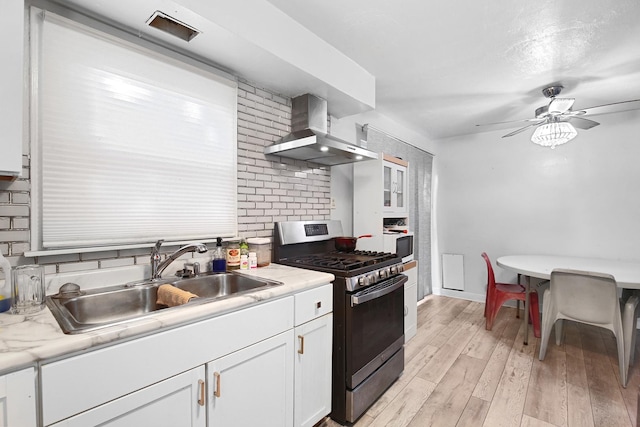 kitchen featuring stainless steel gas stove, wall chimney exhaust hood, sink, light hardwood / wood-style flooring, and white cabinets