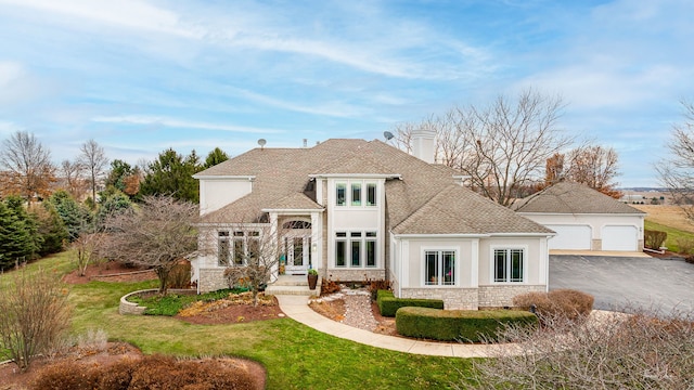 view of front of home featuring a garage, stone siding, an outdoor structure, a front yard, and roof with shingles