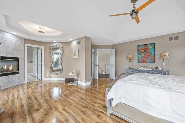 bedroom featuring wood finished floors, a tray ceiling, a tiled fireplace, visible vents, and recessed lighting