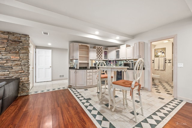 kitchen featuring stainless steel microwave, dark countertops, visible vents, light wood-style floors, and open shelves
