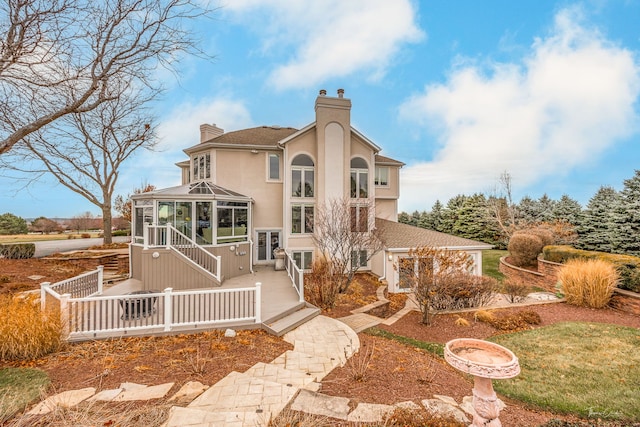 rear view of house featuring a sunroom, a chimney, and stucco siding