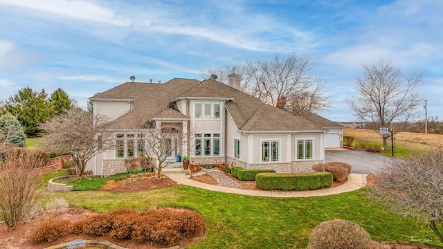 rear view of property featuring stone siding, a lawn, a shingled roof, and stucco siding