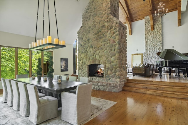 dining space featuring a stone fireplace, beamed ceiling, high vaulted ceiling, light hardwood / wood-style floors, and wood ceiling