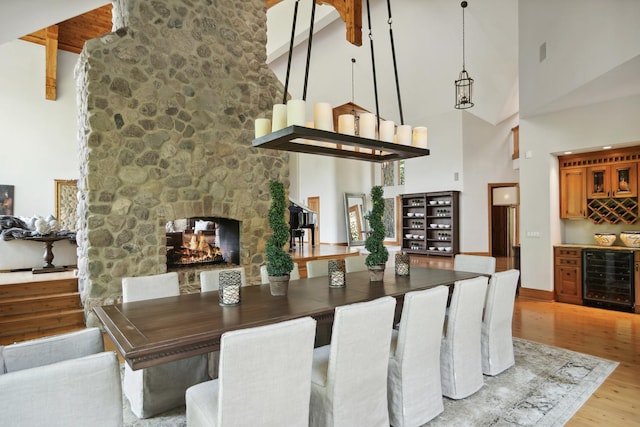 dining space with high vaulted ceiling, bar area, light hardwood / wood-style floors, wine cooler, and a stone fireplace