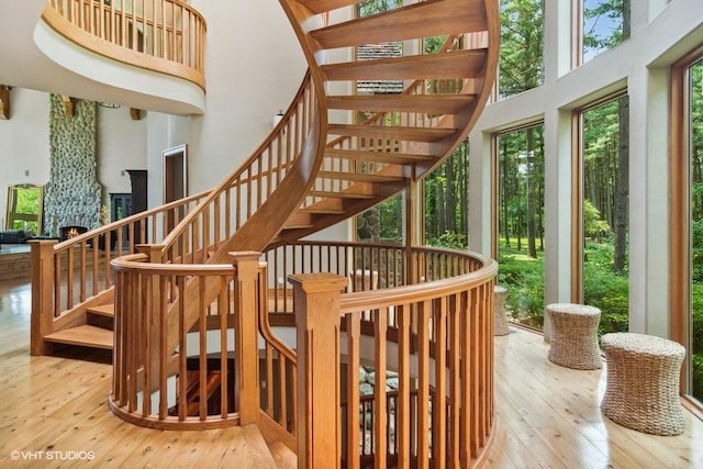 staircase with hardwood / wood-style flooring, a towering ceiling, and a fireplace