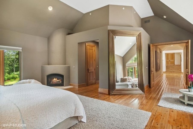 bedroom featuring a fireplace, hardwood / wood-style floors, and high vaulted ceiling