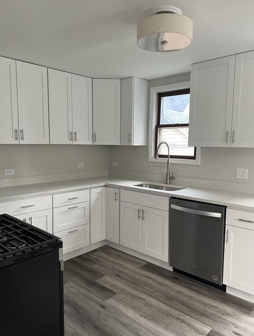 kitchen featuring stainless steel dishwasher, dark wood-type flooring, sink, range, and white cabinetry