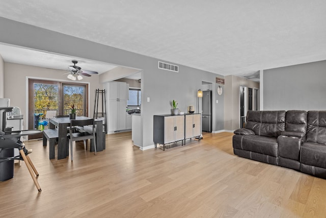 living room with a textured ceiling, light hardwood / wood-style flooring, and ceiling fan