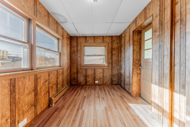 empty room with a baseboard radiator, a drop ceiling, and light hardwood / wood-style flooring