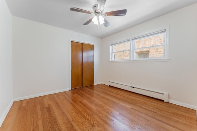 unfurnished bedroom featuring a closet, a baseboard heating unit, ceiling fan, and light hardwood / wood-style flooring