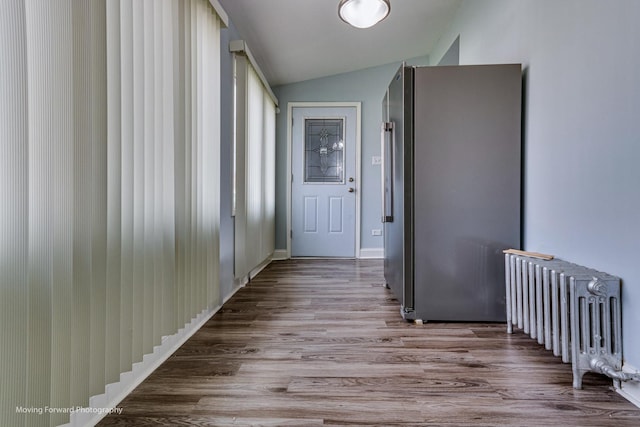 corridor with radiator heating unit, light hardwood / wood-style floors, and lofted ceiling