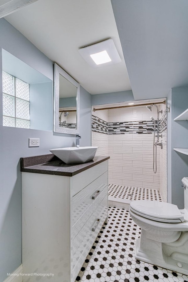 bathroom featuring toilet, a tile shower, and vanity