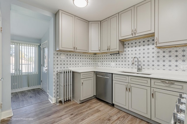 kitchen featuring radiator heating unit, light wood-type flooring, stainless steel dishwasher, and sink