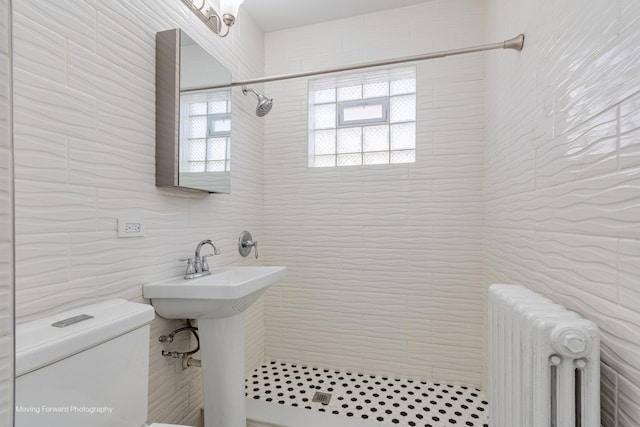 bathroom featuring tiled shower, radiator heating unit, toilet, and tile walls