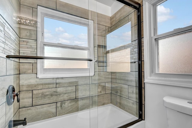 bathroom with toilet and shower / bath combination with glass door