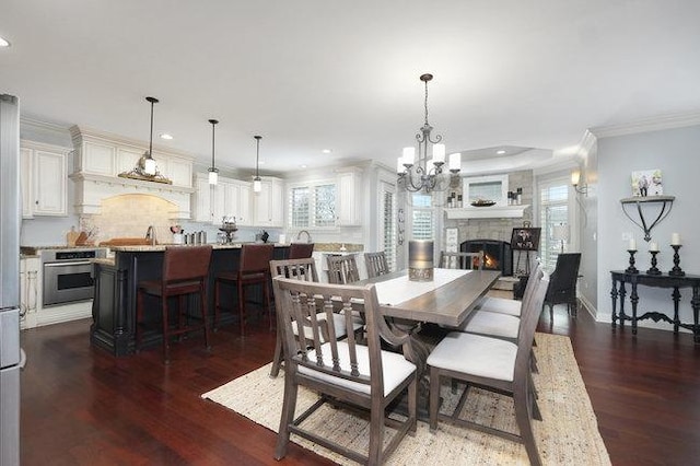 dining room with dark hardwood / wood-style flooring, a stone fireplace, crown molding, and an inviting chandelier