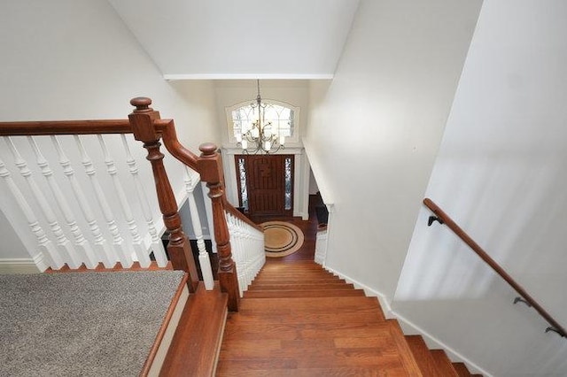 staircase featuring hardwood / wood-style flooring, vaulted ceiling, and an inviting chandelier