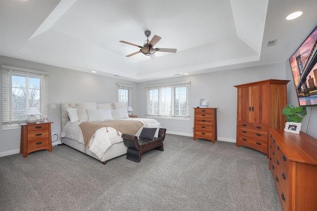 carpeted bedroom with multiple windows, a tray ceiling, and ceiling fan