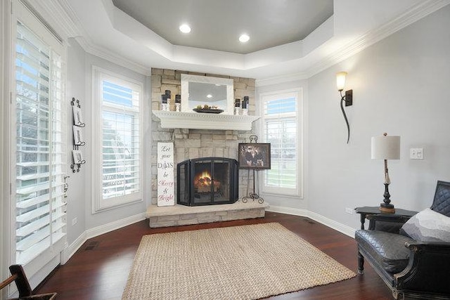 living room with a tray ceiling, crown molding, a fireplace, and dark wood-type flooring