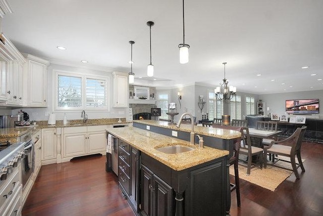 kitchen featuring a kitchen breakfast bar, light stone counters, sink, white cabinets, and an island with sink