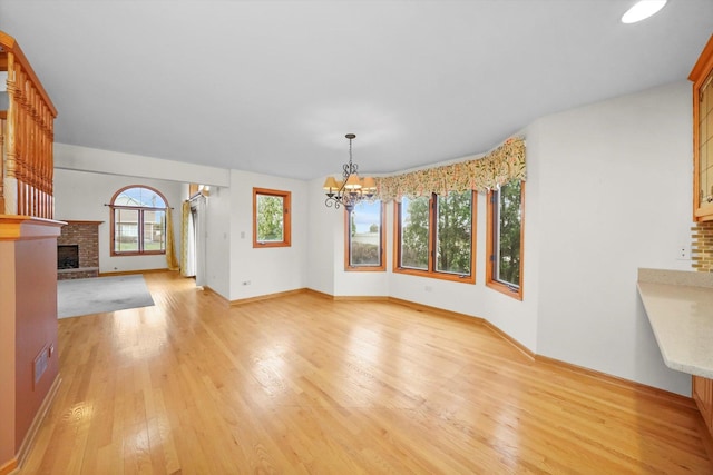 unfurnished living room featuring a wealth of natural light, light hardwood / wood-style flooring, a chandelier, and a brick fireplace