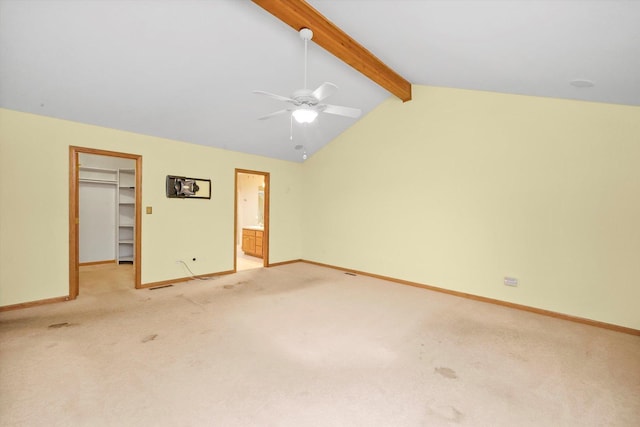 unfurnished bedroom featuring a walk in closet, vaulted ceiling with beams, ceiling fan, connected bathroom, and light colored carpet