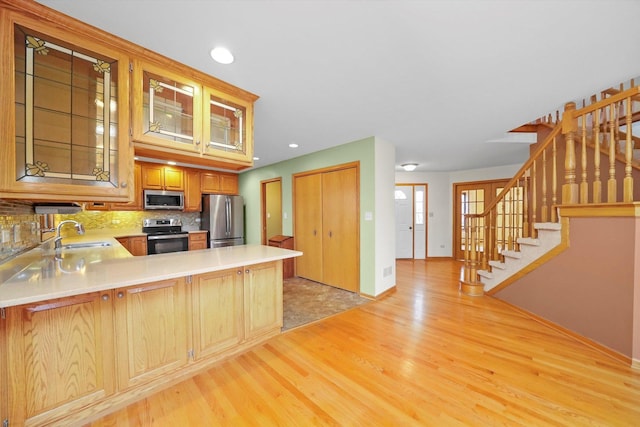 kitchen with kitchen peninsula, appliances with stainless steel finishes, decorative backsplash, sink, and light hardwood / wood-style floors