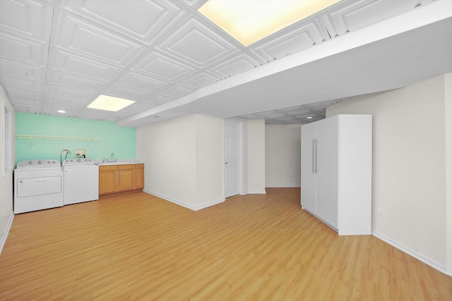 basement featuring washer and dryer, light hardwood / wood-style flooring, and sink