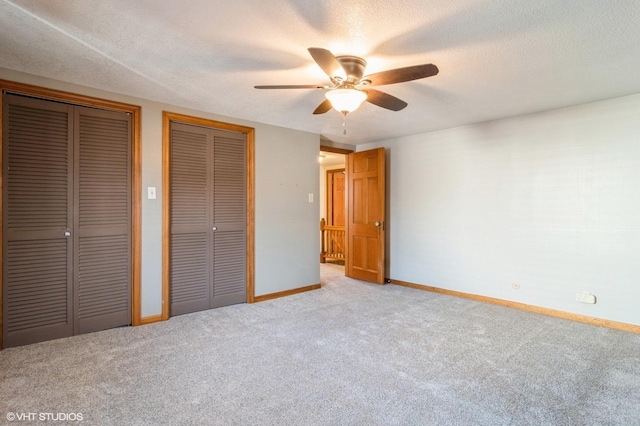 unfurnished bedroom featuring a textured ceiling, ceiling fan, light carpet, and two closets