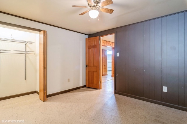 unfurnished bedroom featuring wooden walls, a closet, ceiling fan, and crown molding