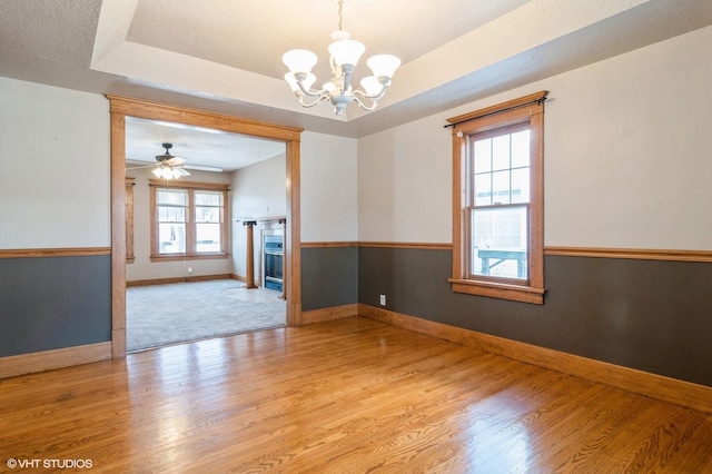 unfurnished room with ceiling fan with notable chandelier, a tray ceiling, and light hardwood / wood-style floors