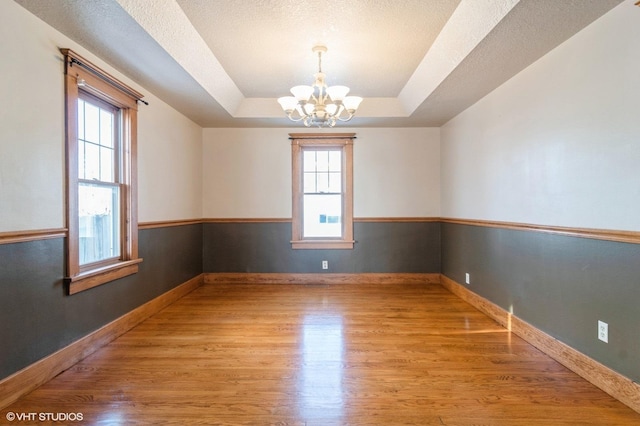 spare room featuring a raised ceiling, plenty of natural light, light hardwood / wood-style flooring, and a notable chandelier