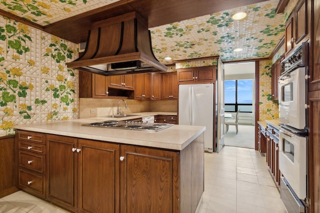 kitchen featuring white appliances, sink, custom range hood, light tile patterned flooring, and kitchen peninsula