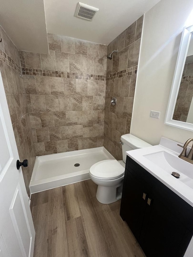 bathroom featuring wood-type flooring, vanity, a tile shower, and toilet