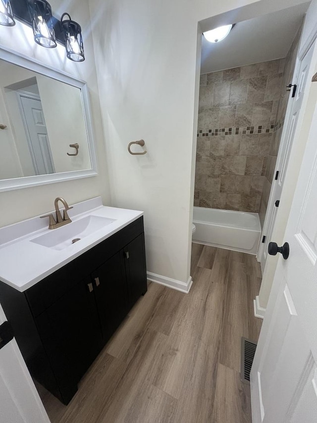 full bathroom featuring hardwood / wood-style floors, vanity, tiled shower / bath combo, and toilet