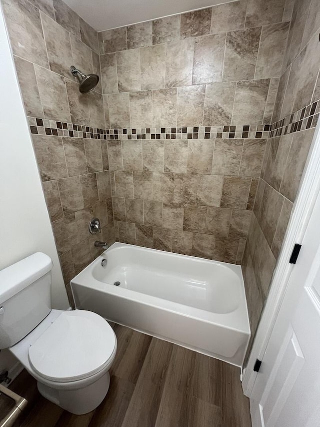 bathroom with hardwood / wood-style floors, toilet, and tiled shower / bath