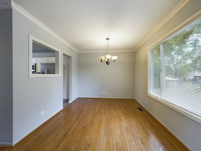 empty room featuring hardwood / wood-style floors, crown molding, and a chandelier