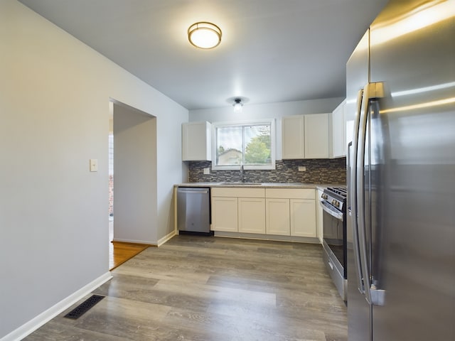 kitchen with decorative backsplash, appliances with stainless steel finishes, sink, hardwood / wood-style flooring, and white cabinetry