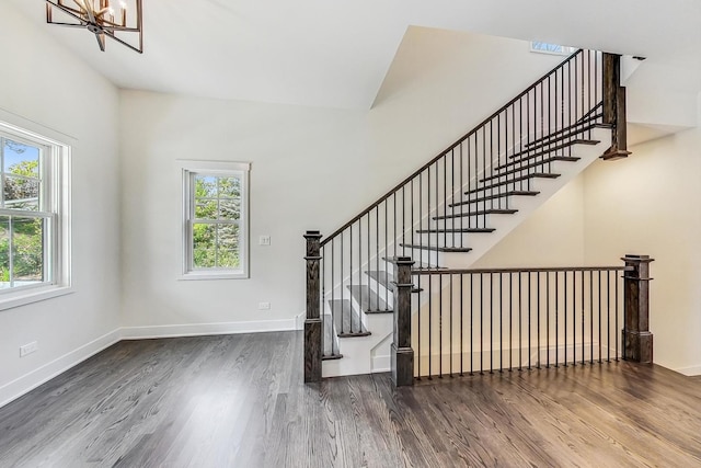 stairway featuring a wealth of natural light, an inviting chandelier, baseboards, and wood finished floors