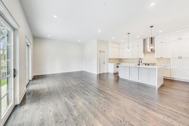 kitchen with pendant lighting, light countertops, white cabinetry, wall chimney range hood, and an island with sink