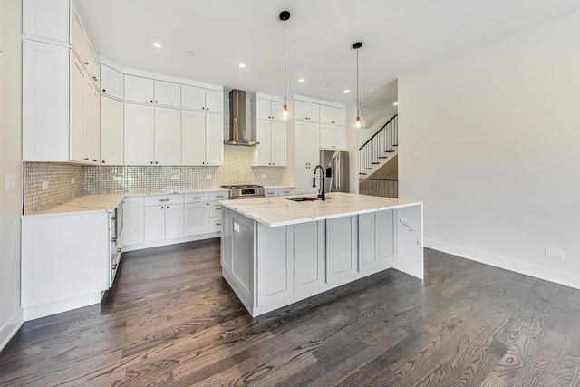 kitchen featuring hanging light fixtures, a kitchen island with sink, wall chimney range hood, white cabinetry, and a sink