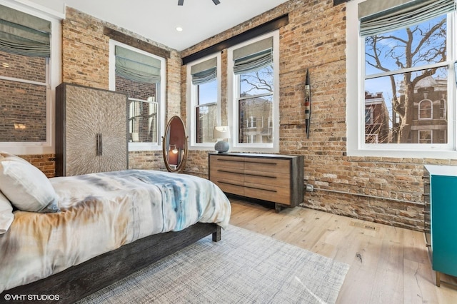 bedroom with ceiling fan, wood-type flooring, and brick wall