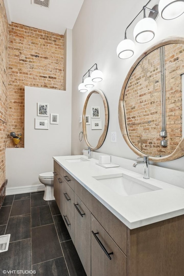 bathroom with vanity, toilet, and brick wall