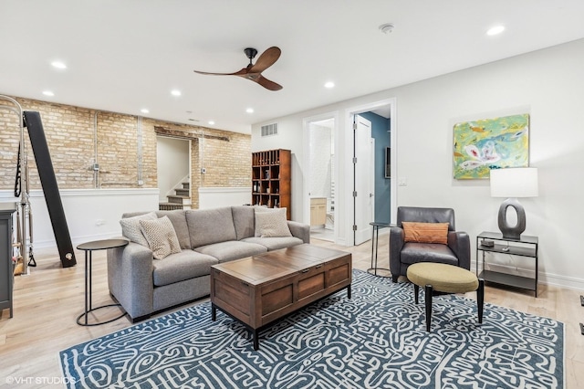 living room with light hardwood / wood-style floors, ceiling fan, and brick wall