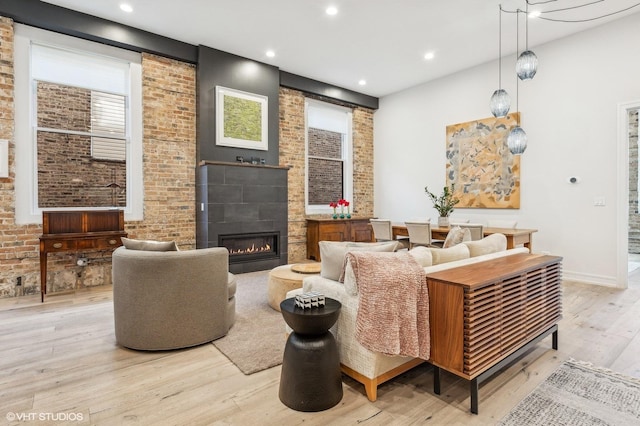 living room with a tile fireplace, light hardwood / wood-style floors, and brick wall