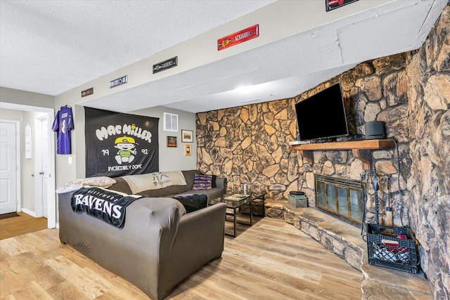 living room featuring hardwood / wood-style flooring, a stone fireplace, and a textured ceiling