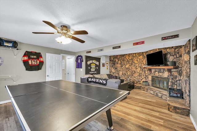 playroom featuring ceiling fan, a fireplace, wood-type flooring, and a textured ceiling