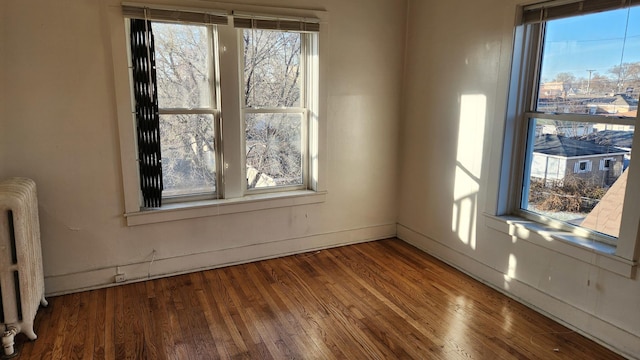 unfurnished room featuring radiator heating unit, a healthy amount of sunlight, and wood-type flooring