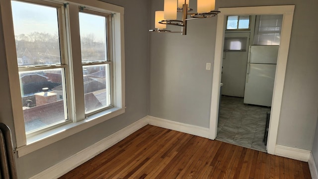 unfurnished dining area with dark wood-type flooring, a wealth of natural light, and an inviting chandelier